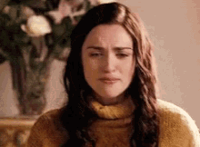 a woman in a yellow sweater is making a funny face in front of a vase of flowers .