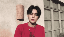 a young man wearing a red shirt and a necklace is standing in front of a building