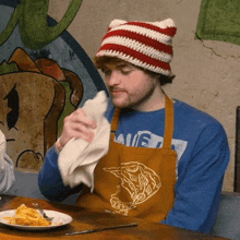 a man wearing an apron and a hat wipes his face with a napkin