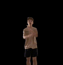 a boy is standing in front of a black background and covering his mouth with his hand ..