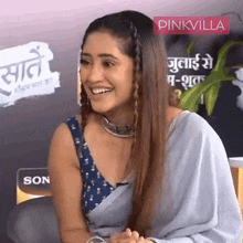 a woman in a blue saree is smiling in front of a pinkvilla sign