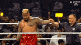 a man in red shorts is standing in a wrestling ring with a referee holding his hand