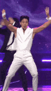 a man in a white shirt and white pants is dancing on a stage with his arms outstretched .