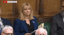 a woman in a blue jacket is sitting in front of a group of people with the words live the commons on the bottom