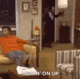 a man is sitting on a couch in a living room while a man in a suit stands in the doorway .