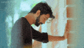 a man with a beard is leaning against a wall with his hand on it