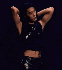 a man is standing on a stage with his hands behind his head and a crop top on .