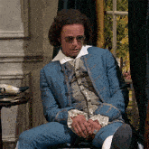 a man wearing a blue jacket and a white shirt sits in front of a window