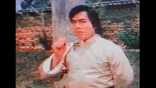 a man in a white shirt is standing in front of a stone wall with his fist up .