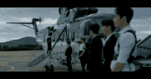 a group of men in suits are standing in front of a helicopter .