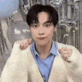 a young man in a blue shirt and a white sweater is standing in front of balloons .