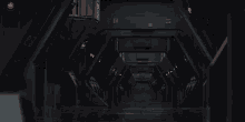 a long dark hallway with red lights on the walls and a red light on the ceiling .