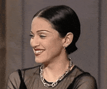 a woman wearing a chain necklace and earrings smiles