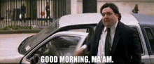 a man in a suit and tie is standing next to a car and says `` good morning , ma am '' .