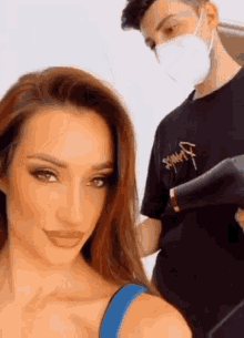 a man wearing a mask is drying a woman 's hair