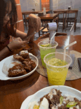 a woman sits at a table with a plate of food and two cups of drinks