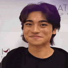 a young man with purple hair and a black shirt is smiling .