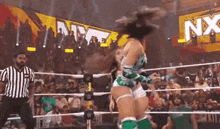 a woman is jumping in the air in a wrestling ring while a referee looks on .