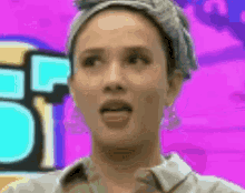 a woman wearing a headband and earrings is sticking her tongue out in front of a pink background .