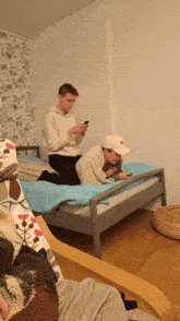 two boys sit on a bed looking at their cell phones