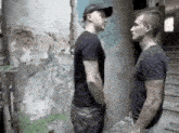 two men are standing next to each other in front of a wall and talking .