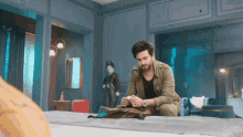 a man is sitting on a bed in a room with a statue of charlie chaplin in the background