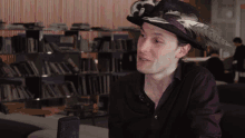 a man wearing a hat with feathers on it is sitting in front of a microphone