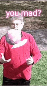 a man in a red shirt is holding a pink ball in front of his face with the words you mad behind him