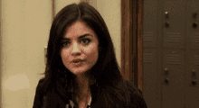 a woman with long dark hair is standing in front of a locker in a locker room .