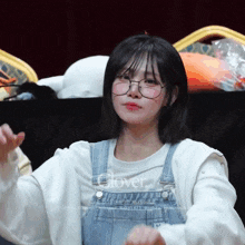 a girl wearing glasses and overalls has the word clover on her sweater