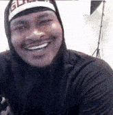 a man wearing a hooded shirt and a hat is smiling .