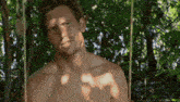 a shirtless man is sitting on a swing in the woods