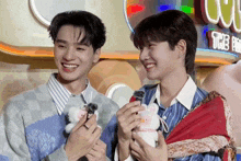two young men are smiling and holding stuffed animals in front of a sign that says tcc