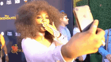 a woman blowing a kiss while taking a selfie in front of a wall that says descendants on it