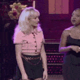 a woman in a pink crop top and black skirt is standing next to another woman in a black dress on a stage .