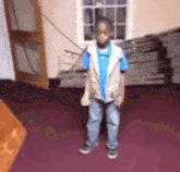 a young boy is standing in a room wearing a blue shirt and a tan vest .