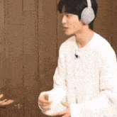 a man wearing headphones and a white sweater is shaking hands with another man .