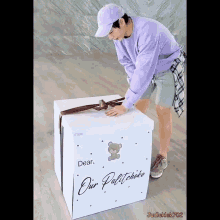 a man in a purple hat is opening a white box that says dear our palitcheke