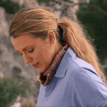 a woman wearing a blue shirt and a scarf around her neck looks down