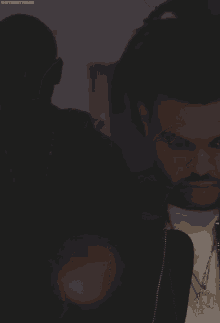 a man with a beard wearing a black jacket and a gold necklace with the letter d on it