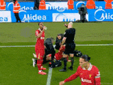 a soccer player is kneeling down on the field while a referee talks to him .