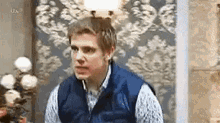 a man in a blue vest is sitting in front of a lamp in a room .