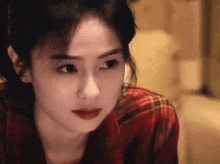 a woman wearing a red plaid shirt looks at the camera