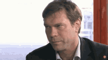 a man in a suit and white shirt looks at the camera with a sticker on his shirt that says ' bbc ' on it