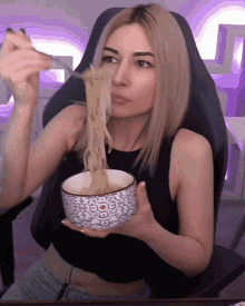 a woman in a black tank top is eating noodles from a bowl