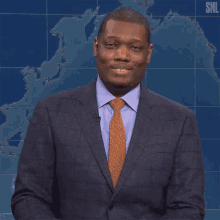 a man in a suit and tie smiles in front of a snl map