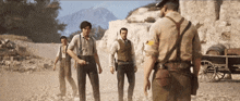 a group of men are standing on a dirt road with a mountain in the background
