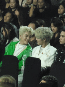 a man in a green jacket sits next to a man in a white suit