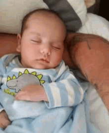 a baby is sleeping on a bed with a dinosaur on his outfit .