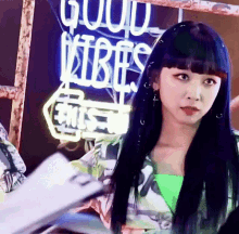 a woman with long black hair is standing in front of a neon sign that says good vibes .